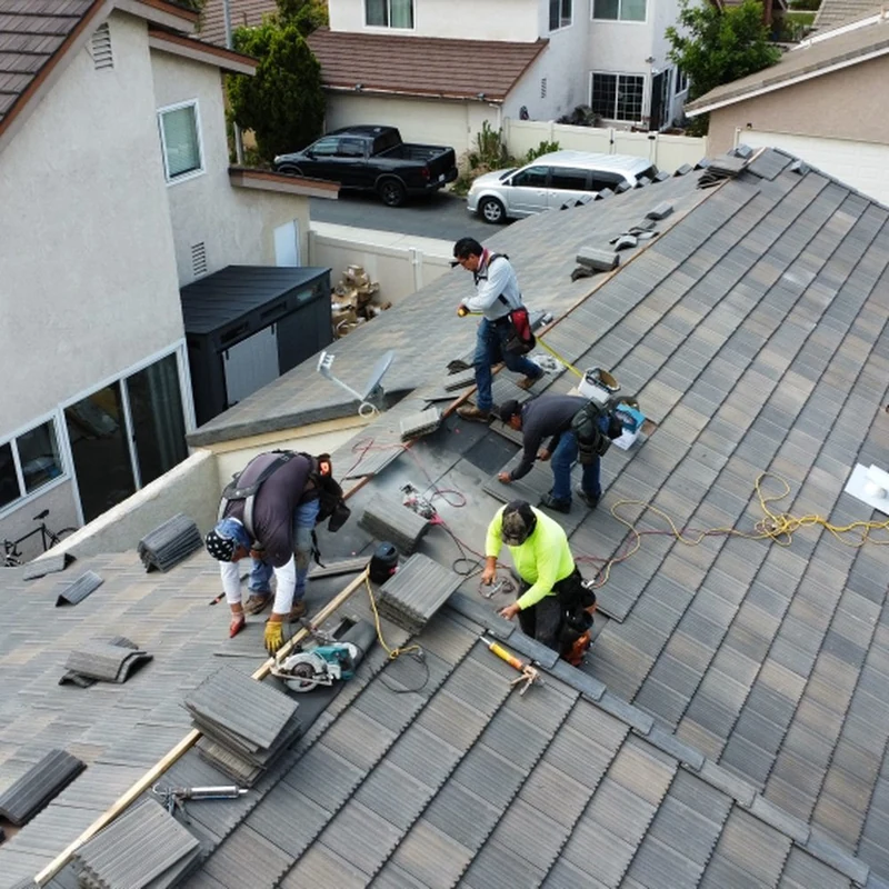 Overhead view of a crew re-laying concrete tiles on a house roof.