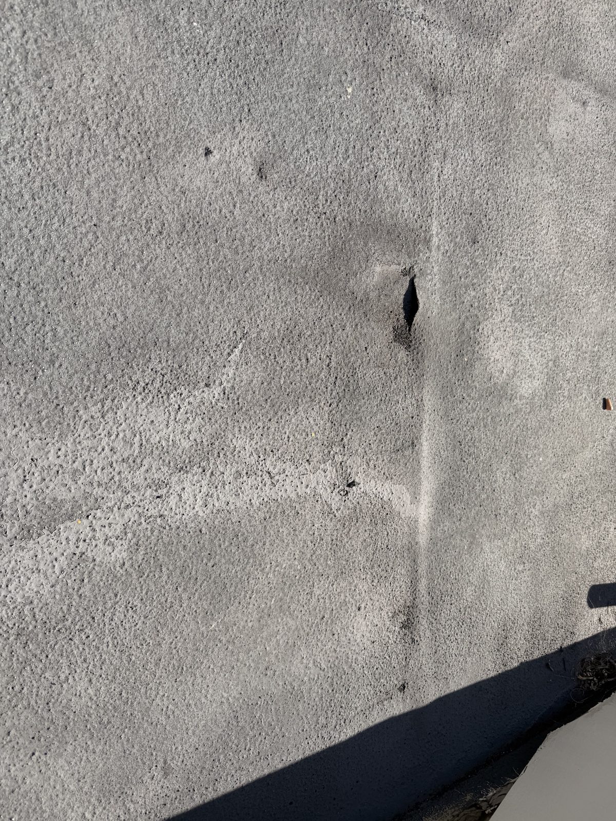 Open split in the gray coating of the low-slope roof section before the failed covering was removed.