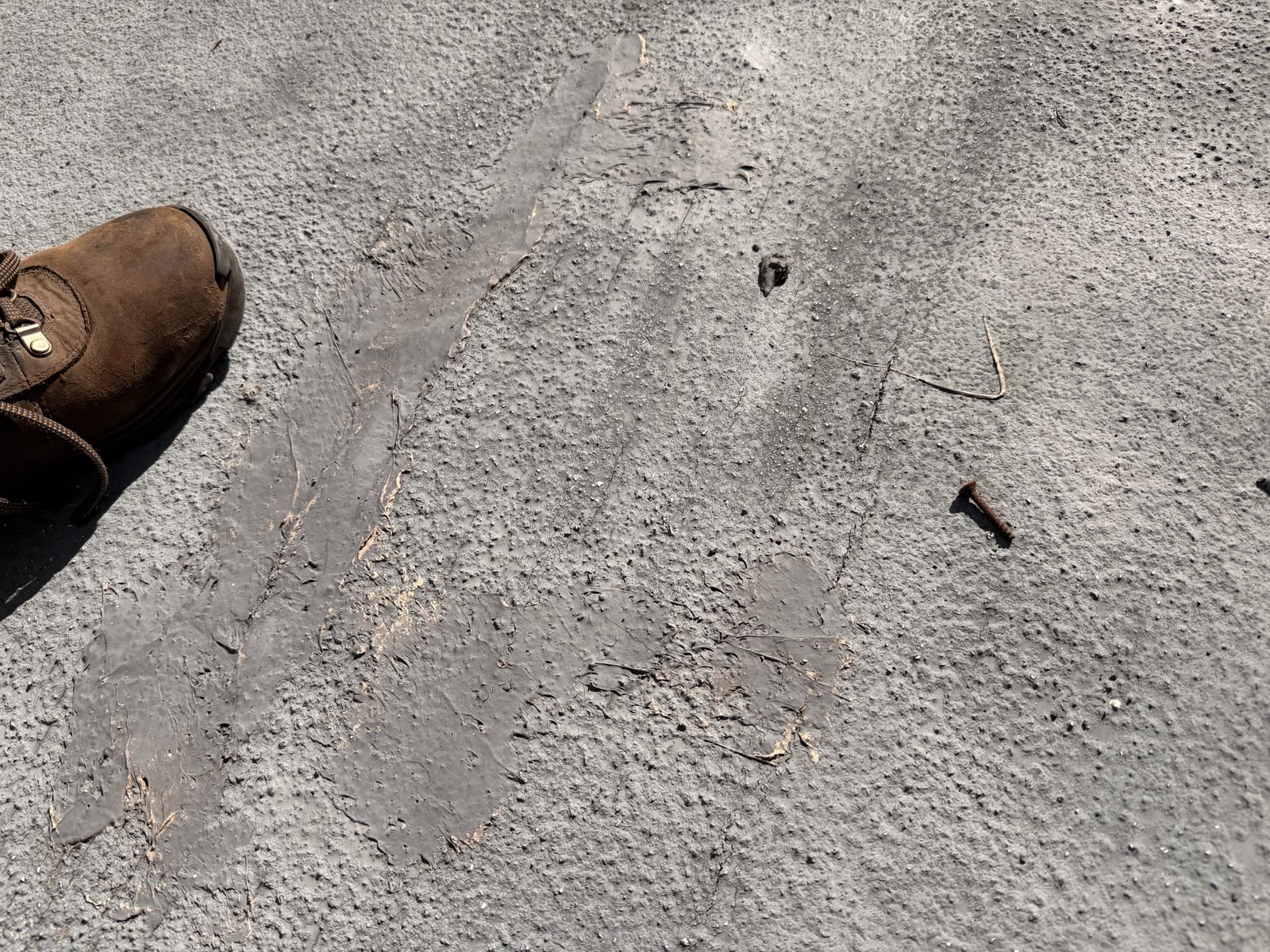 Uneven older roof-cement patches and cracked coating on the flat roof before the new repair.