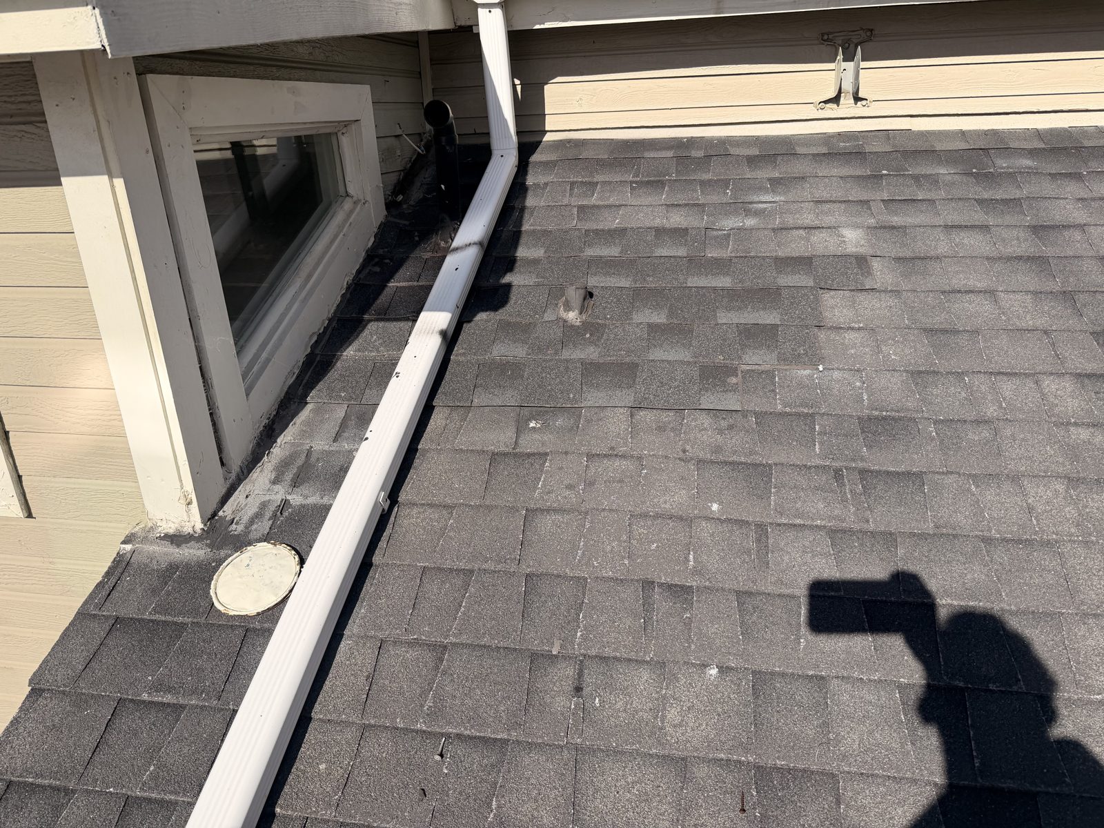White downspout running across the shingle roof beside the dormer window at the Dana Point property.